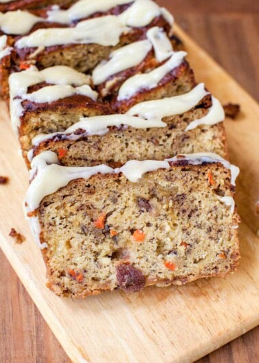 Sliced carrot cake loaf with cream cheese frosting on a wooden board.