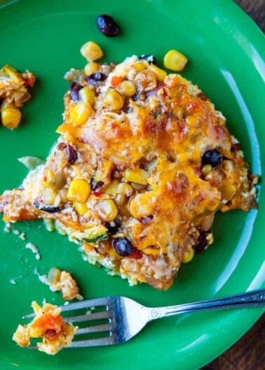 A slice of cheesy casserole with corn and black beans on a green plate with a fork.
