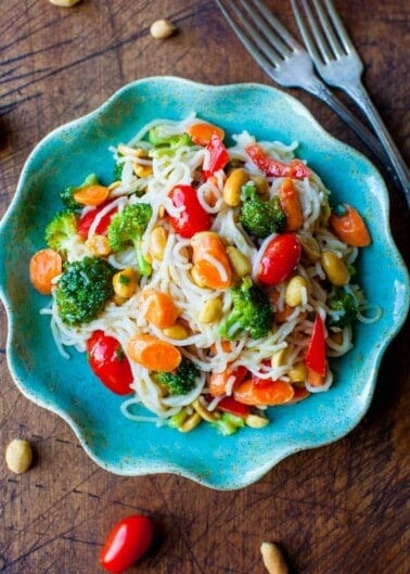 A bowl of rice noodle salad with broccoli, carrots, tomatoes, and peanuts.