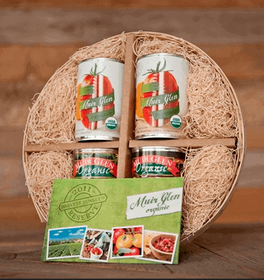 Four cans of organic muir glen tomatoes displayed with decorative straw in a spherical basket, accompanied by a recipe card.