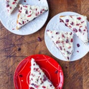Slices of white chocolate bark with cranberries and nuts served on various colored plates.