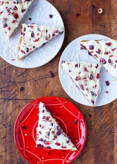 Slices of white chocolate bark with cranberries and nuts served on various colored plates.