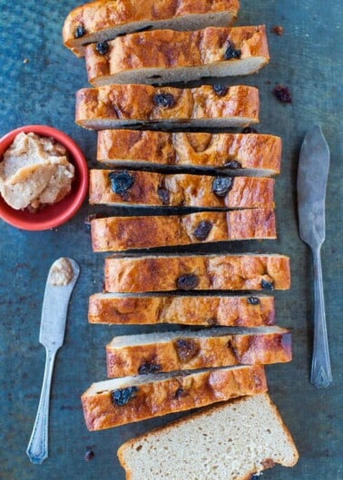 Sliced fruit loaf with butter and a knife on a blue textured surface.