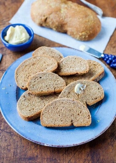 Sliced whole grain bread on a blue plate with butter on the side.