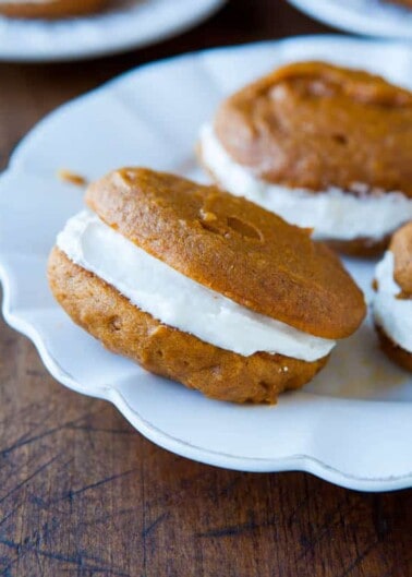 A pumpkin whoopie pie with cream filling on a white plate.