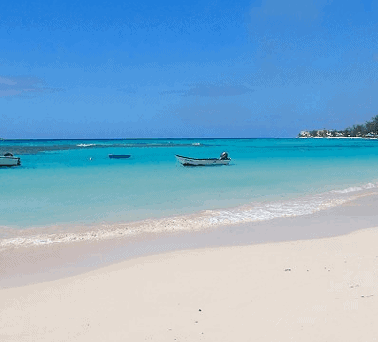 Idyllic tropical beach with clear turquoise waters and several boats anchored near the shore.