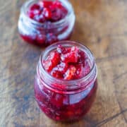 Two jars of homemade cranberry sauce on a wooden surface.