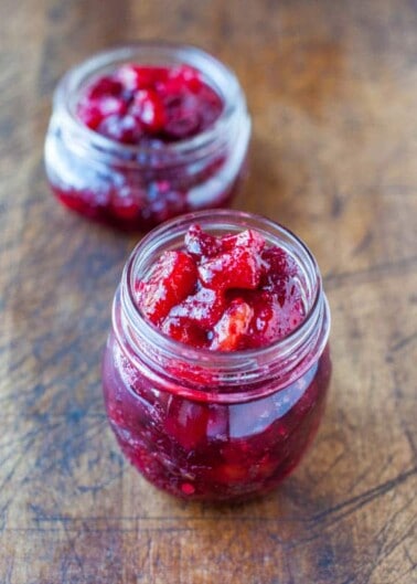 Two jars of homemade cranberry sauce on a wooden surface.