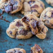 Freshly baked chocolate chip cookies on a baking sheet, some with melting chocolate chunks visible.