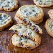 Chocolate chip cookies on a wooden surface, one cookie broken in half to reveal melted chocolate.
