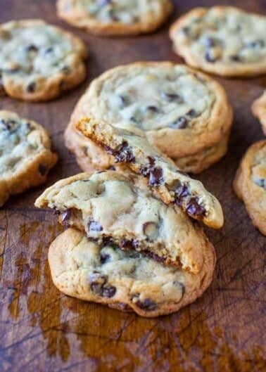 Chocolate chip cookies on a wooden surface, one cookie broken in half to reveal melted chocolate.