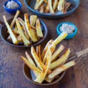 Homemade french fries served in bowls with dipping sauces on a wooden table.