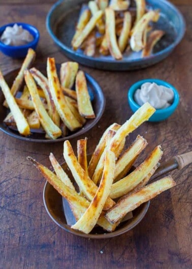 Homemade french fries served in bowls with dipping sauces on a wooden table.