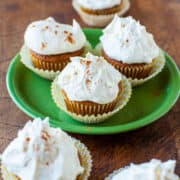 Freshly baked cupcakes with white frosting and a sprinkle of cinnamon on a green plate.