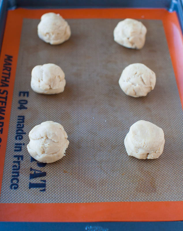 six raw cookie dough balls on a baking sheet 