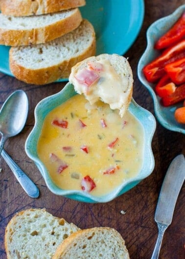 A bowl of creamy soup with red bell peppers, served with sliced baguette on a blue plate.