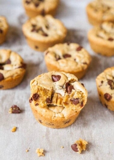 Freshly baked chocolate chip cookies on a surface, with one cookie broken to reveal the soft interior.