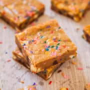 Stack of blondie bars with colorful sprinkles on a wooden surface.