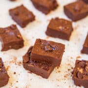 Pieces of chocolate fudge with nuts on parchment paper.