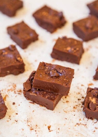 Pieces of chocolate fudge with nuts on parchment paper.