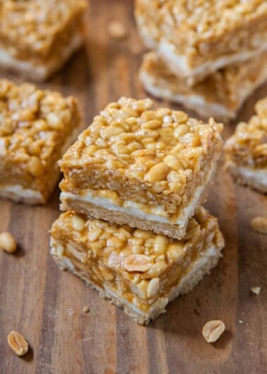 Stacked peanut brittle squares on a wooden surface.