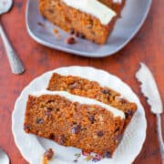 A slice of carrot cake with cream cheese frosting, served on a plate with a fork, with more cake in the background.