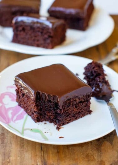 A slice of chocolate cake with glossy icing on a plate, partially eaten.