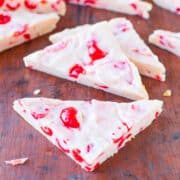 Pieces of cherry and almond white chocolate bark on a wooden surface.