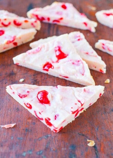 Pieces of cherry and almond white chocolate bark on a wooden surface.