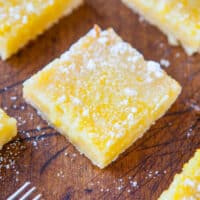 Lemon bars dusted with powdered sugar on a wooden board.