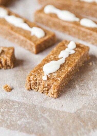 Homemade granola bars with a drizzle of yogurt icing on a parchment paper surface.