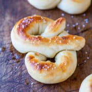 Golden-brown soft pretzels sprinkled with coarse salt on a wooden surface.