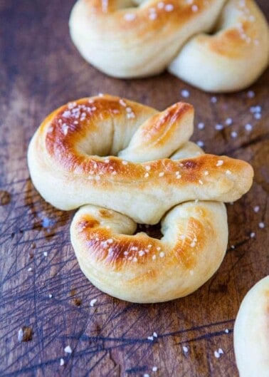 Golden-brown soft pretzels sprinkled with coarse salt on a wooden surface.