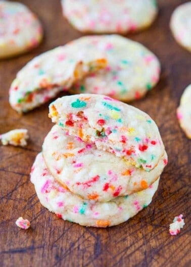 Sugar cookies with colorful sprinkles on a wooden surface.