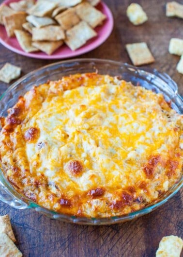 Baked cheesy dip served in a glass dish with crackers on the side.