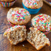 Freshly baked muffins with colorful sprinkles on a wooden surface.