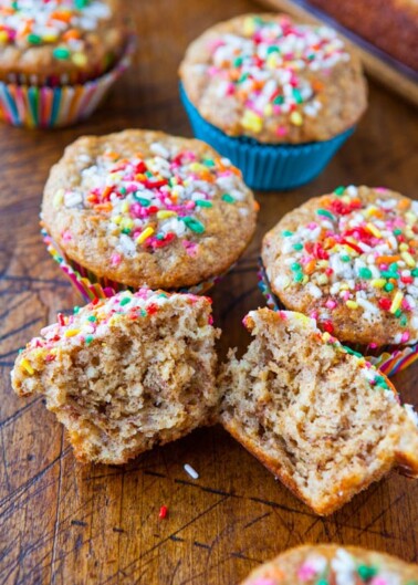 Freshly baked muffins with colorful sprinkles on a wooden surface.