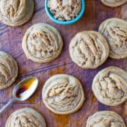 Freshly baked muffins on a wooden surface with a bowl of brown sugar and a spoonful of syrup.