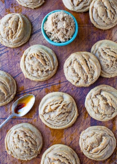 Freshly baked muffins on a wooden surface with a bowl of brown sugar and a spoonful of syrup.