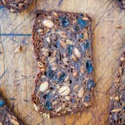 Sliced multi-grain bread with seeds and raisins on a wooden cutting board.