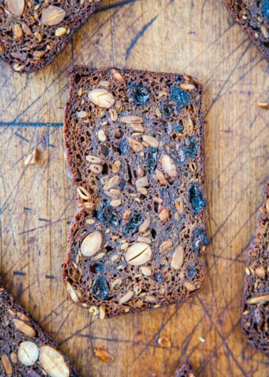 Sliced multi-grain bread with seeds and raisins on a wooden cutting board.