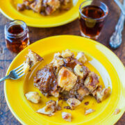 A serving of bread pudding on a yellow plate with a fork, accompanied by small glasses of syrup.