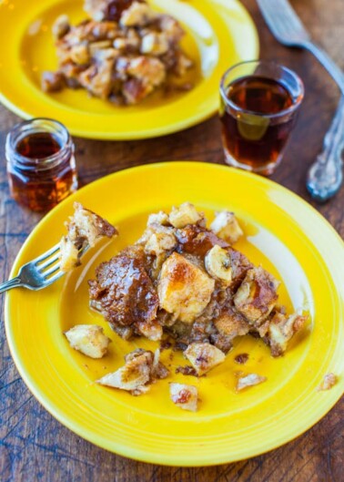 A serving of bread pudding on a yellow plate with a fork, accompanied by small glasses of syrup.