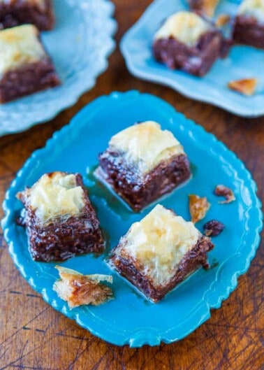 Squares of baklava on a blue plate with additional pieces on a wooden surface.