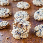 A pile of oatmeal raisin cookies on a wooden surface with one cookie on top having a bite taken out of it.