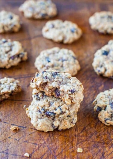 A pile of oatmeal raisin cookies on a wooden surface with one cookie on top having a bite taken out of it.