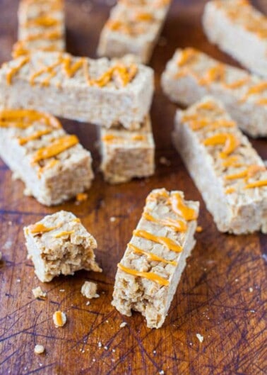 Homemade cereal bars drizzled with peanut butter on a wooden surface.