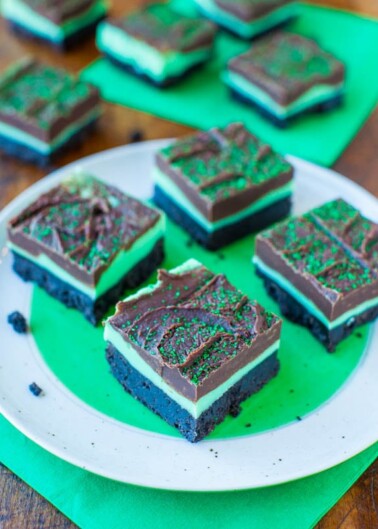 A plate of layered mint chocolate brownies with green sprinkles on a wooden table.