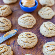 Freshly baked peanut butter cookies on a wooden surface with a dish of peanut butter and a knife.