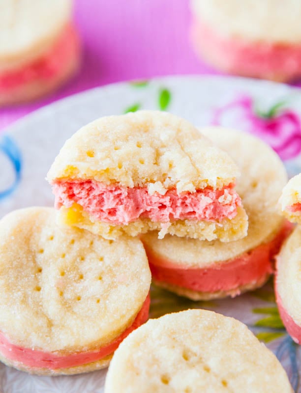 buttery sandwich cookies on a floral plate. The top cookie has a bite missing. 